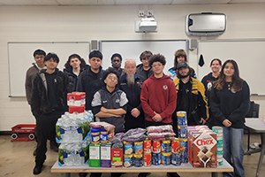 Photo of students standing in front of a food drive table with donations