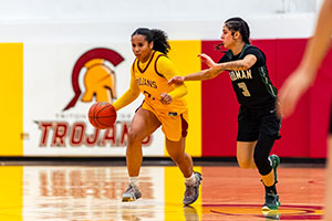 Photo of Female Basketball Player drippling ball down the court while being blocked by opposing player