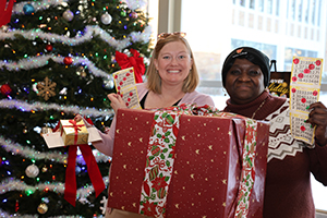 Photo of Staff holding a giant present box in front of Cafeteria Christmas Tree