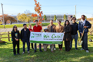Photo of President Moore standing with staff and students posing into front of a Tree Campus Banner
