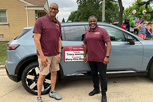 Photo of employees posing in front of blue car